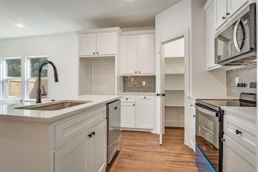 Kitchen featuring appliances with stainless steel finishes, backsplash, white cabinetry, light wood-style floors, and light stone counters