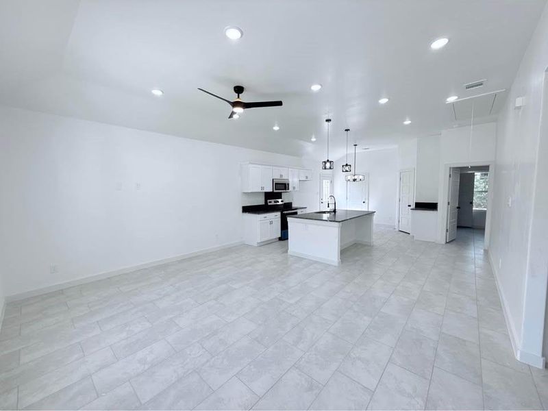 Kitchen with open floor plan, dark countertops, white cabinetry, appliances with stainless steel finishes, and decorative light fixtures Kitchen with open floor plan, dark countertops, white cabinetry, appliances with stainless steel finishes, and decorative light fixtures