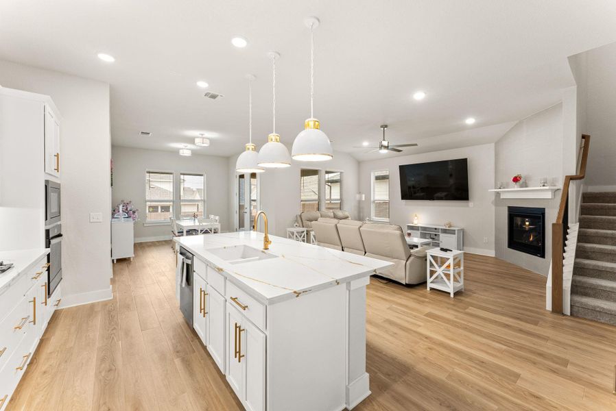 The island kitchen has Silestone counters, 42” Shaker style cabinets with gold hardware, pendant lights, breakfast bar, tile backsplash and walk-in pantry. The stainless steel appliances include a five-burner cooktop, oven, microwave, dishwasher, and vent hood.