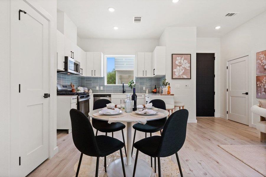 The property features an open-concept living space with light-colored flooring, a modern kitchen with white cabinetry, stainless steel appliances, and a blue tile backsplash, and recessed lighting throughout