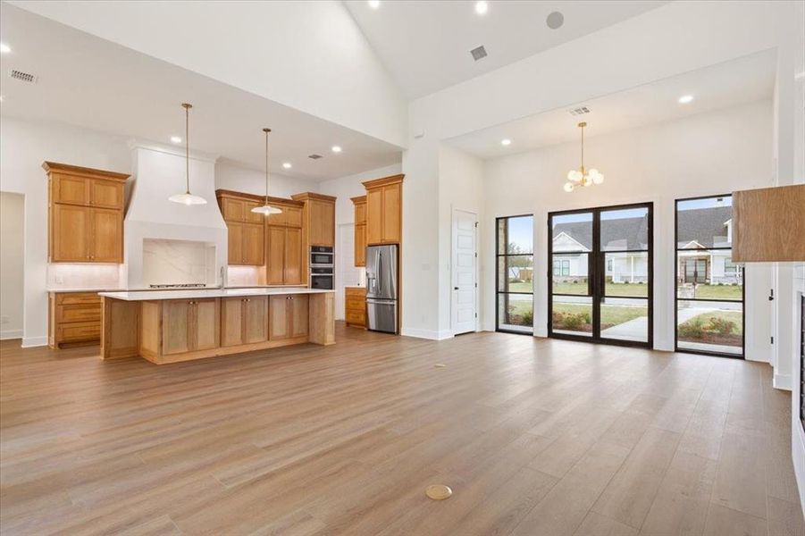 Kitchen featuring open floor plan, high vaulted ceiling, a spacious island, light countertops, and a chandelier