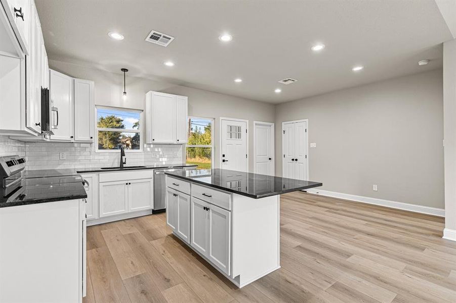 Kitchen featuring dark stone countertops, recessed lighting, a center island, white cabinets, and decorative light fixtures Kitchen featuring dark stone countertops, recessed lighting, a center island, white cabinets, and decorative light fixtures