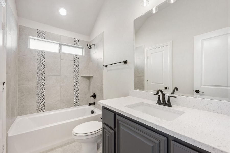 Bathroom with gray tile tub surround, white soaking tub, dark vanity with quartz countertop, and vaulted ceiling Bathroom with gray tile tub surround, white soaking tub, dark vanity with quartz countertop, and vaulted ceiling