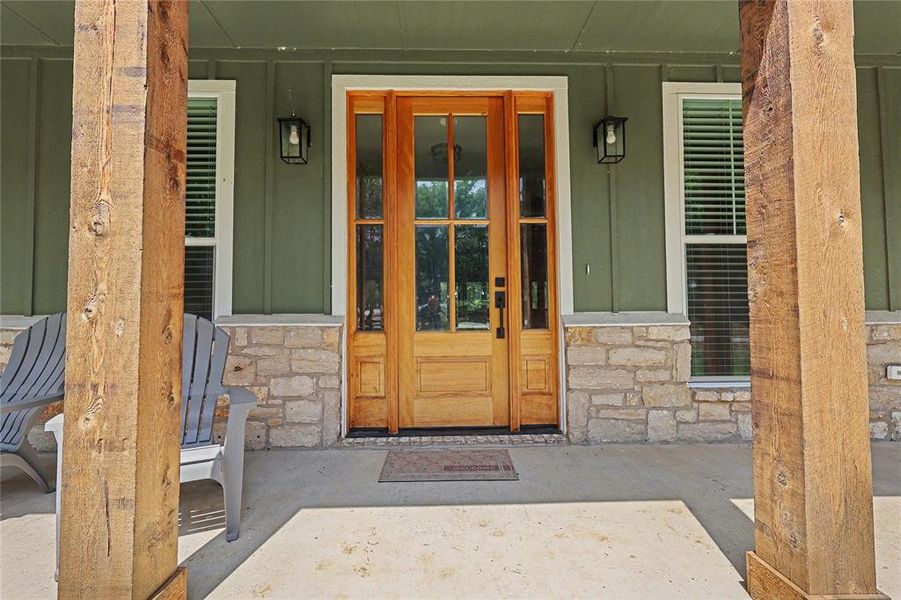 Front porch featuring a wood-paneled door with sidelights, two windows with louvered blinds, and stone facade accents