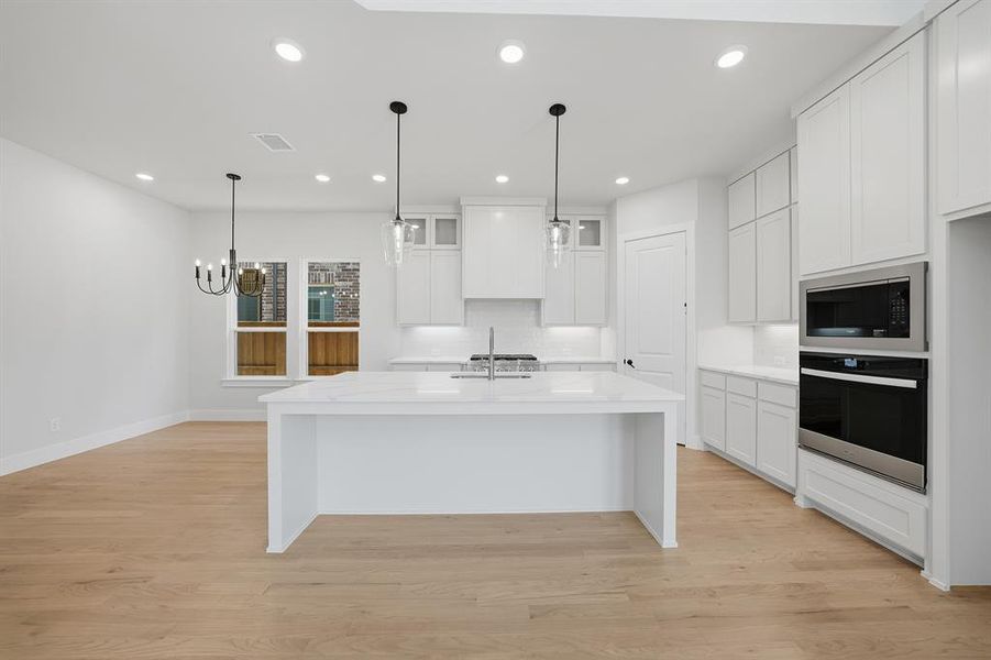 Kitchen with light stone countertops, a kitchen bar, backsplash, white cabinets, and pendant lighting