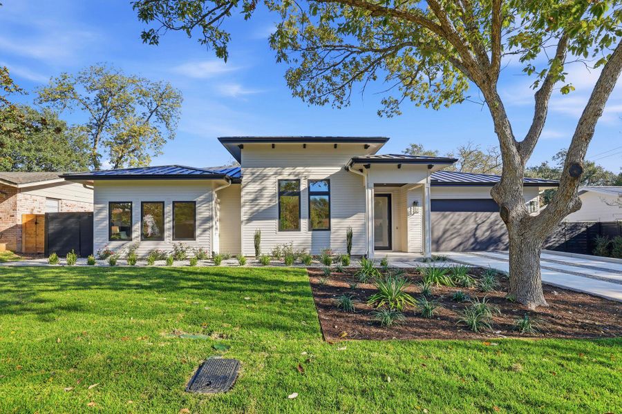 View of front of home featuring a metal roof, a standing seam roof, a front yard, driveway, and a garage