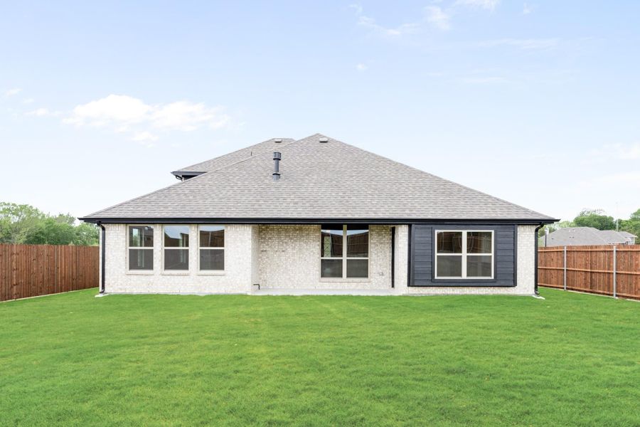 Rear exterior of single-story brick home with gray roof, large windows, and fenced backyard with green lawn