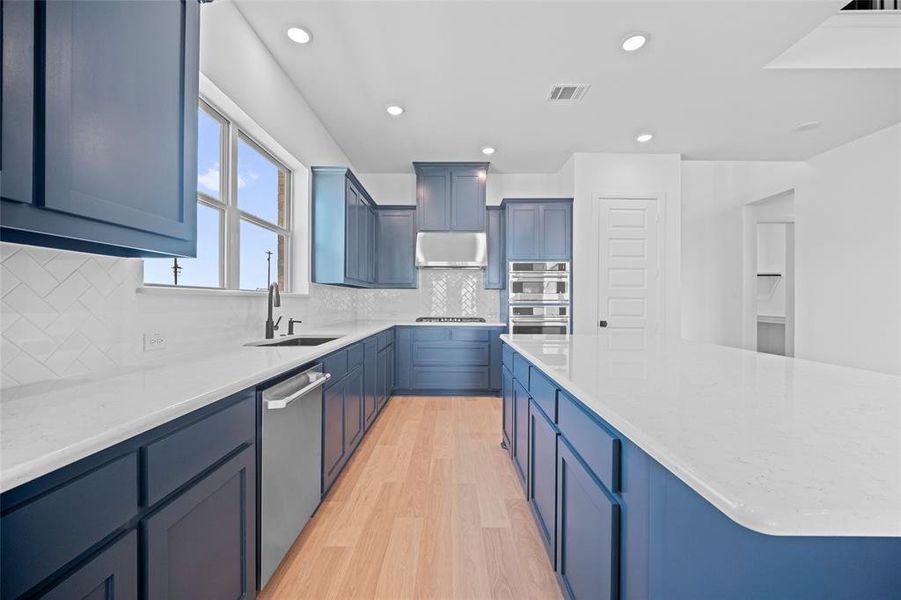 Kitchen featuring light hardwood / wood-style flooring, backsplash, light stone countertops, sink, and stainless steel appliances