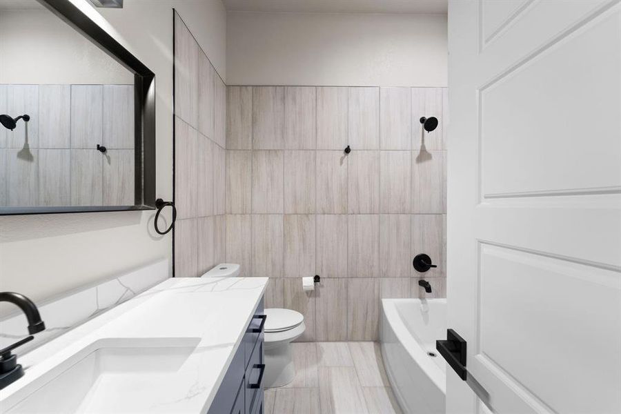 Full bathroom with vanity, tile walls, tiled shower / bath combo, tile patterned flooring, and toilet