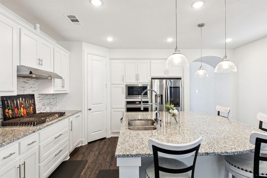 Kitchen with a kitchen bar, light stone counters, white cabinetry, hanging light fixtures, and appliances with stainless steel finishes Kitchen with a kitchen bar, light stone counters, white cabinetry, hanging light fixtures, and appliances with stainless steel finishes