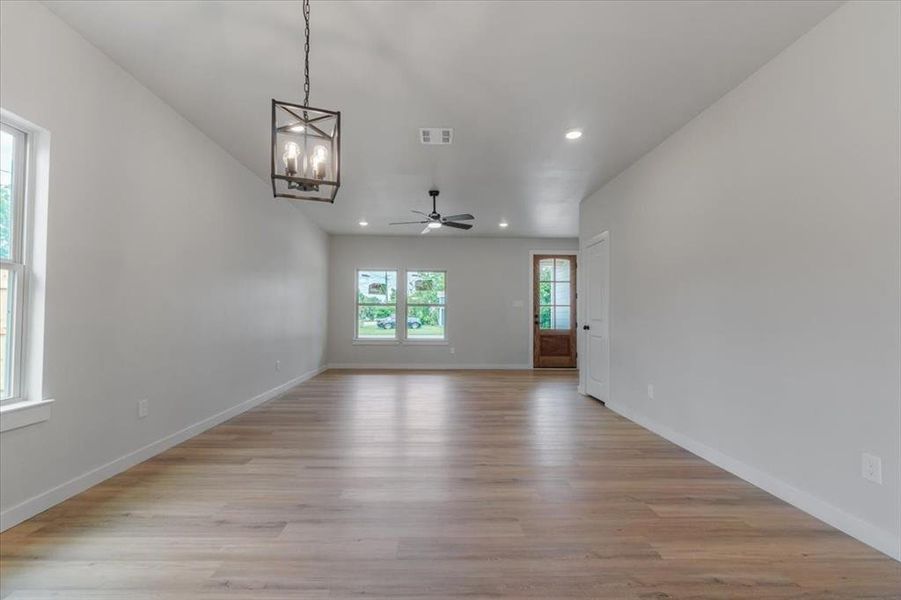 Spare room featuring ceiling fan with notable chandelier and light hardwood / wood-style floors