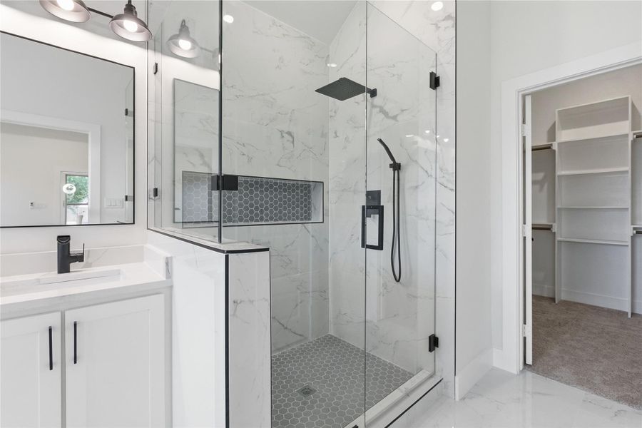Full bathroom with light marble finish flooring, a spacious closet, a marble finish shower, and vanity