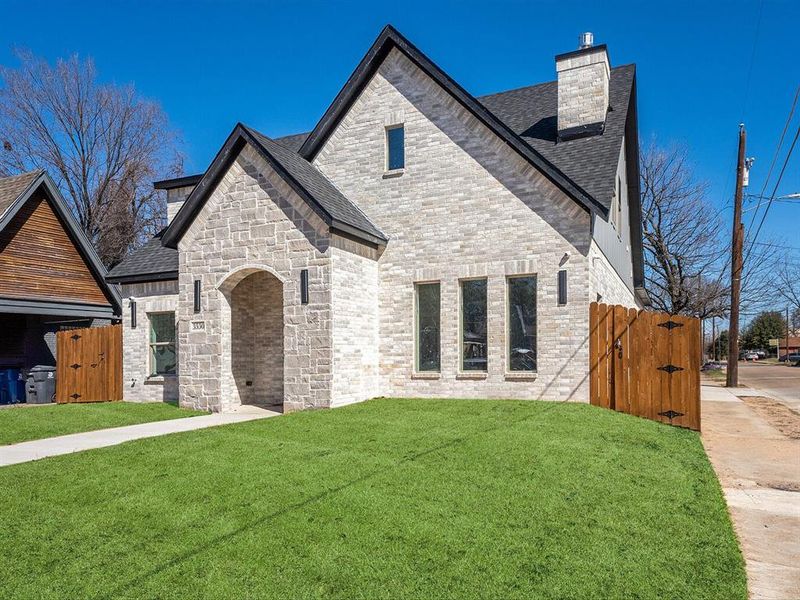 French country style house with a chimney, roof with shingles, a gate, a front lawn, and brick siding