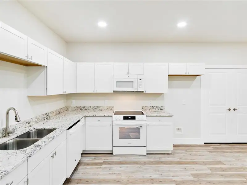 Bright kitchen featuring white cabinetry, stone-finish countertops, stainless steel double basin sink, white range, and wood-finish flooring Bright kitchen featuring white cabinetry, stone-finish countertops, stainless steel double basin sink, white range, and wood-finish flooring