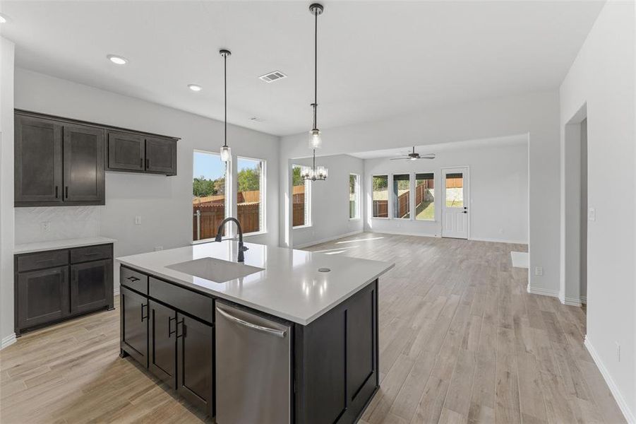Kitchen featuring dishwasher, light wood finished floors, a chandelier, and a kitchen island with sink