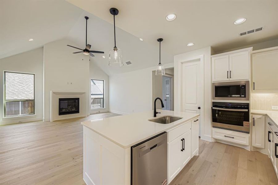 Kitchen with stainless steel appliances, an island with sink, hanging light fixtures, a glass covered fireplace, and open floor plan