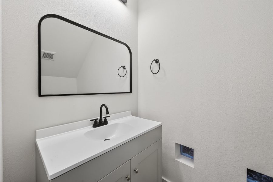Modern powder room with a sleek white vanity, black faucet, and a large rectangular mirror. Minimalist design with white walls and a small window for natural light.