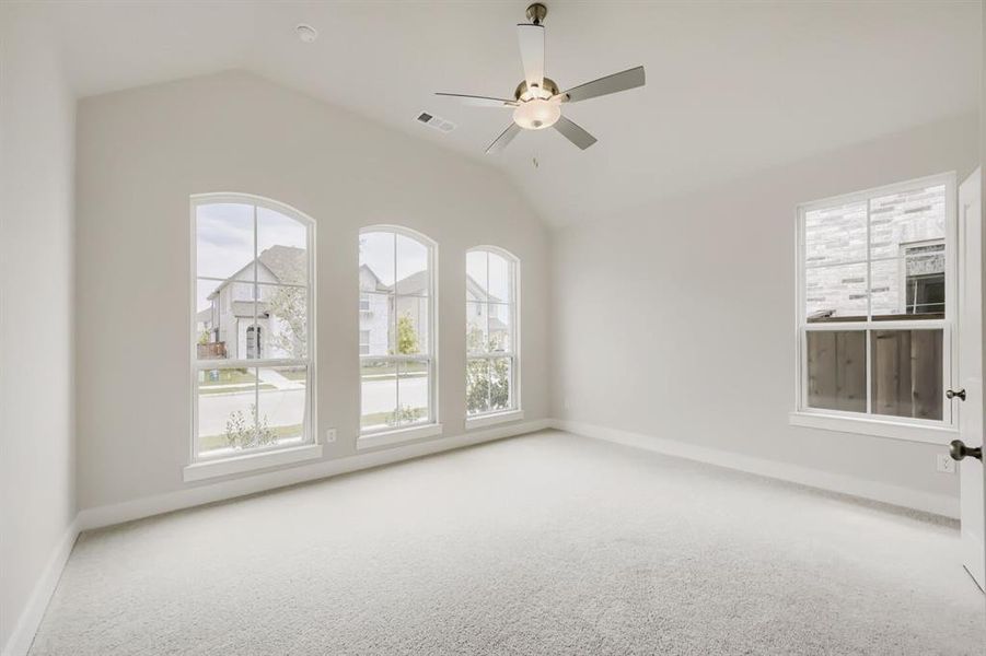 Vaulted ceiling with a contemporary ceiling fan, arched windows, light-toned carpeting, white baseboards, and neutral wall paint