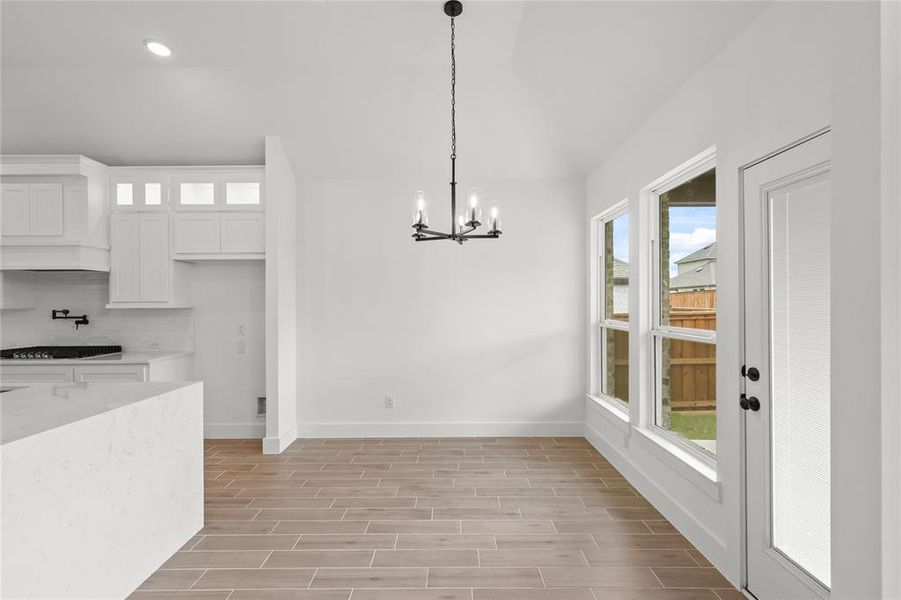 Unfurnished dining area with a wealth of natural light, lofted ceiling, a chandelier, and light wood-type flooring