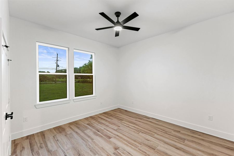 This secondary bedroom features a clean, modern design with light wood-like flooring, bright white walls, and a ceiling fan. Large windows offer plenty of natural light and a view of the outdoors, creating a spacious and inviting atmosphere. This secondary bedroom features a clean, modern design with light wood-like flooring, bright white walls, and a ceiling fan. Large windows offer plenty of natural light and a view of the outdoors, creating a spacious and inviting atmosphere.
