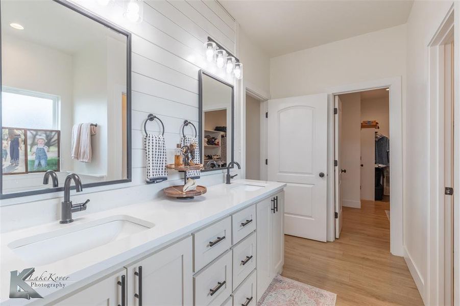 Full bath featuring double vanity, light wood-style flooring, and a walk in closet Full bath featuring double vanity, light wood-style flooring, and a walk in closet