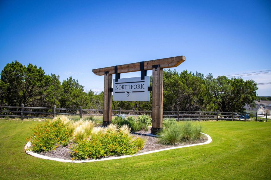 Welcoming community entry with a robust wooden sign, lush green lawn, and vibrant landscaping.