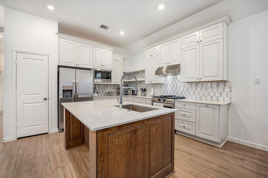 This modern kitchen features white cabinetry, stainless steel appliances, and a central island with a sleek countertop. The open layout flows into a dining area with ample natural light from a large window. This modern kitchen features white cabinetry, stainless steel appliances, and a central island with a sleek countertop. The open layout flows into a dining area with ample natural light from a large window.