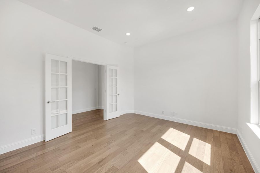 Empty room with hardwood floors, white walls, and double French doors leading to an adjacent space