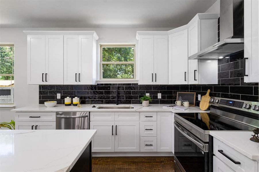 Kitchen featuring appliances with stainless steel finishes, wall chimney exhaust hood, decorative backsplash, and white cabinetry Kitchen featuring appliances with stainless steel finishes, wall chimney exhaust hood, decorative backsplash, and white cabinetry