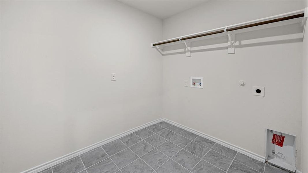 Utility room featuring grey square tile flooring, white baseboards, a single clothing rod, and a built-in shelf