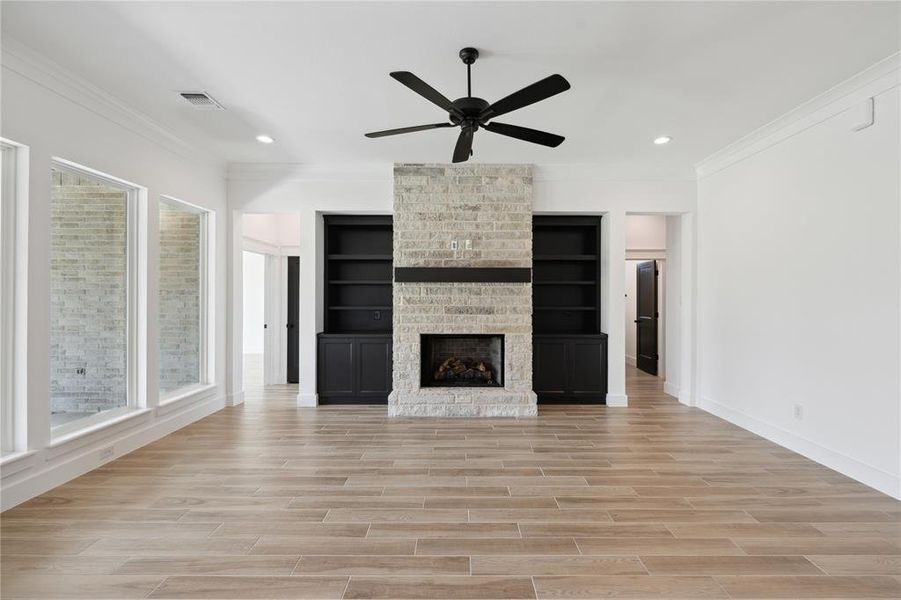 Unfurnished living room featuring a fireplace, light wood-type flooring, ornamental molding, and ceiling fan