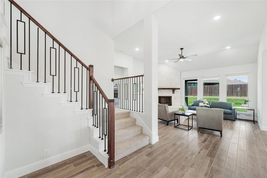 Open living area with staircase, wood-look floors, stone fireplace, and ceiling fan Open living area with staircase, wood-look floors, stone fireplace, and ceiling fan