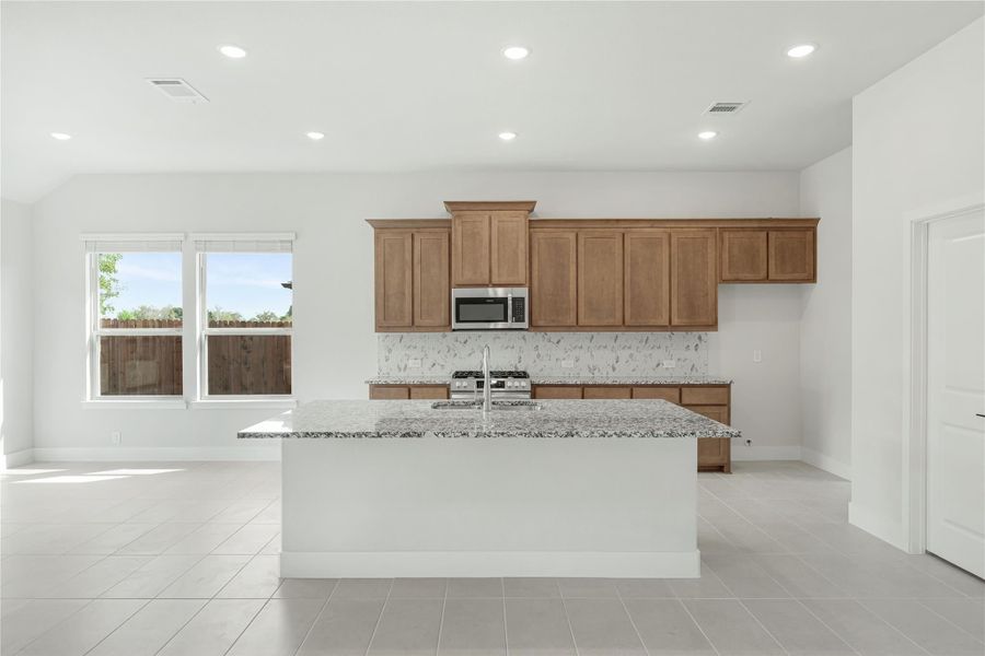 Kitchen with large granite island, wood cabinets, tile backsplash, and stainless steel microwave