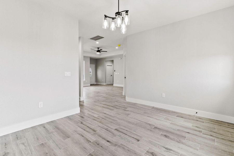 This photo showcases a bright, modern interior with light wood flooring, neutral gray walls, and recessed lighting. The room features a contemporary light fixture and a ceiling fan, giving it a sleek and airy feel. Ideal for an open and inviting living space.