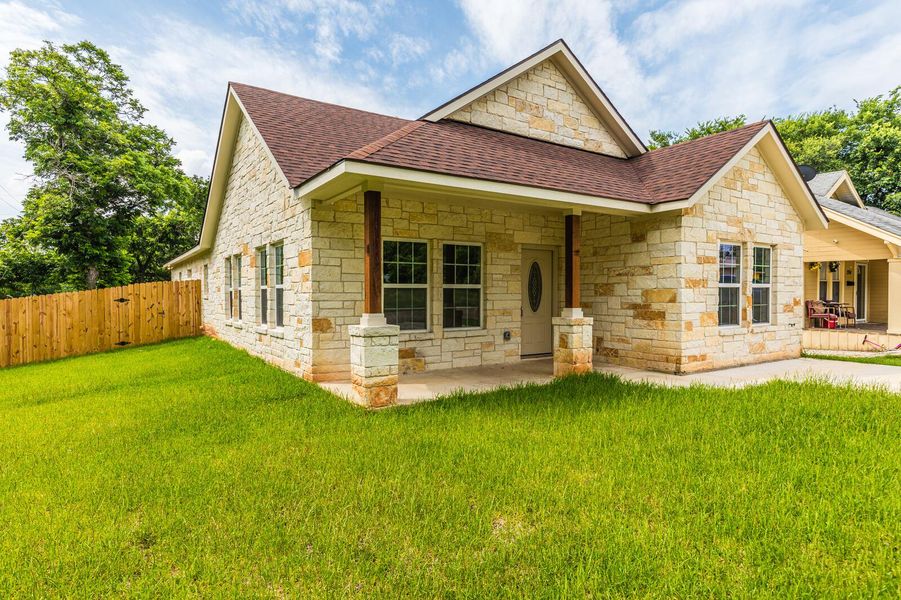 View of front facade with a shingled roof, stone siding, and a patio area