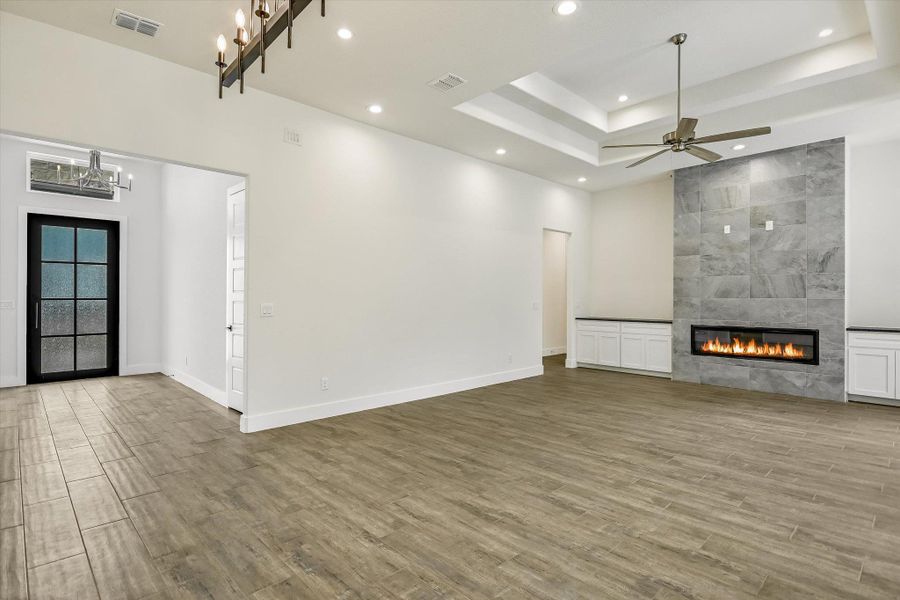 Unfurnished living room with a tiled fireplace, light wood-type flooring, hanging lights, ceiling fan, and a raised ceiling