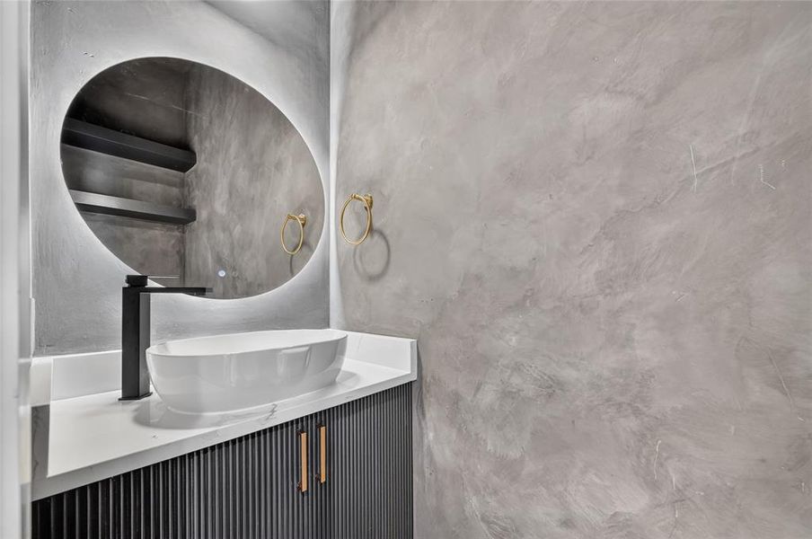 Modern vanity featuring a white vessel sink, matte black faucet, and a lighted oval mirror Modern vanity featuring a white vessel sink, matte black faucet, and a lighted oval mirror