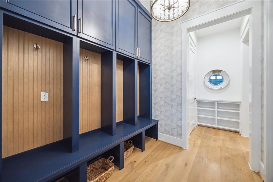 This serene mud room features custom wallpaper, a bench, storage cabinets, hooks and designer lighting.