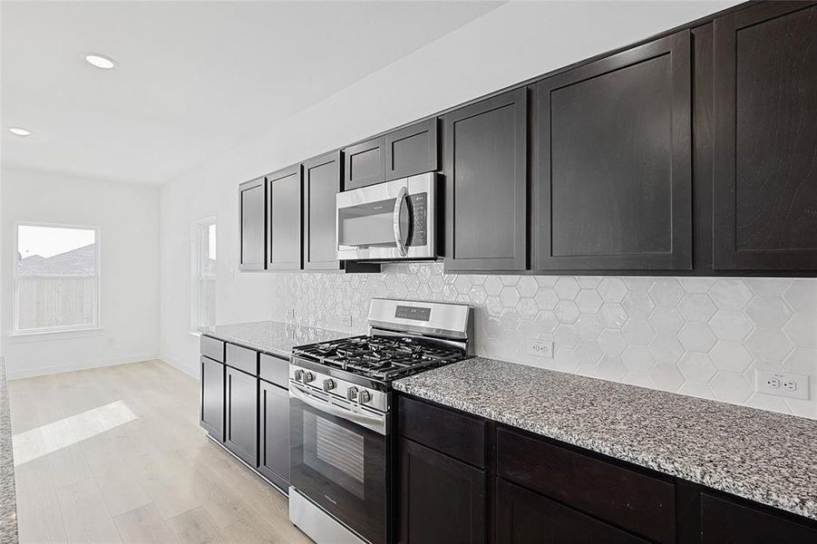 Kitchen featuring tasteful backsplash, light stone countertops, stainless steel appliances, and light hardwood / wood-style floors