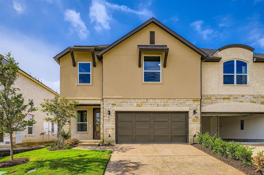 View of front of home with stone siding, an attached garage, driveway, and stucco siding