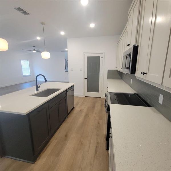 Kitchen with ceiling fan, light hardwood / wood-style flooring, stainless steel appliances, hanging light fixtures, and sink