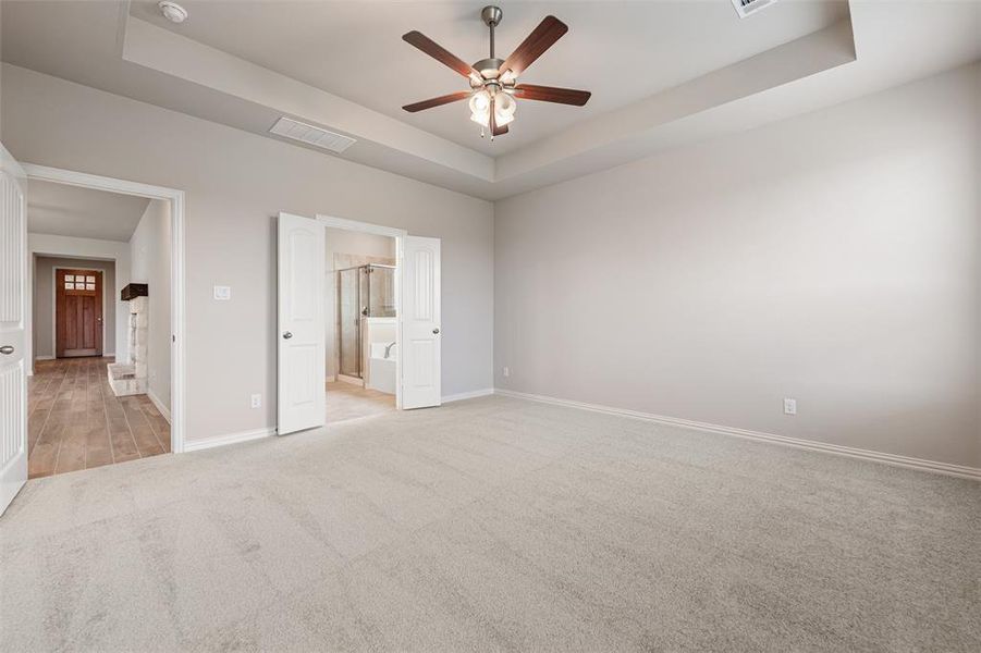 Unfurnished bedroom with a tray ceiling, light carpet, a ceiling fan, and connected bathroom Unfurnished bedroom with a tray ceiling, light carpet, a ceiling fan, and connected bathroom