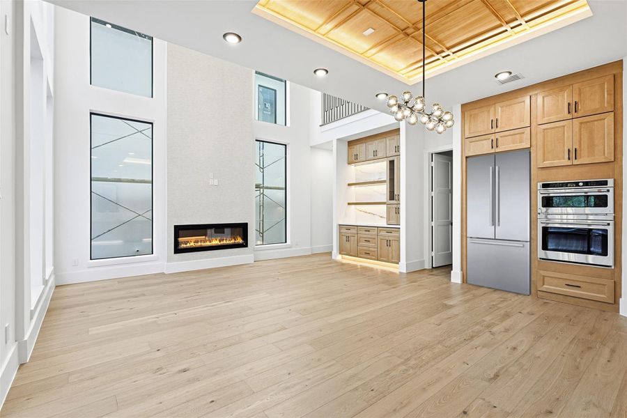 The double-height living area includes a linear gas fireplace and a recessed wood-coffered ceiling feature.