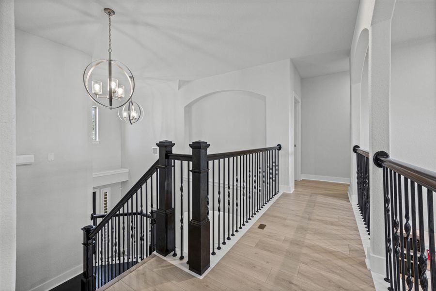 Elegant ironwork banisters guide the way up this refined staircase, featuring natural light and decorative arched wall accents.