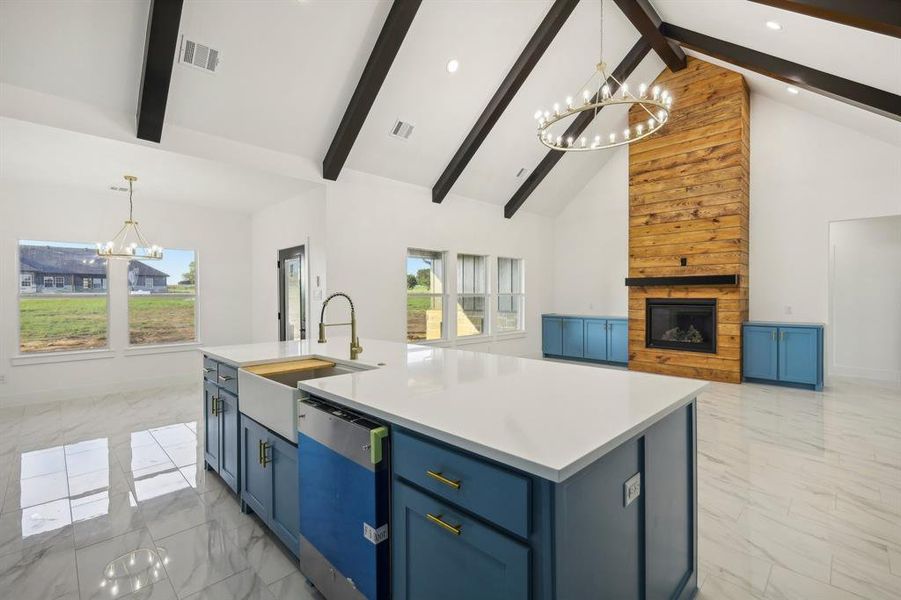 Kitchen with dishwasher, a center island with sink, sink, a notable chandelier, and a large fireplace