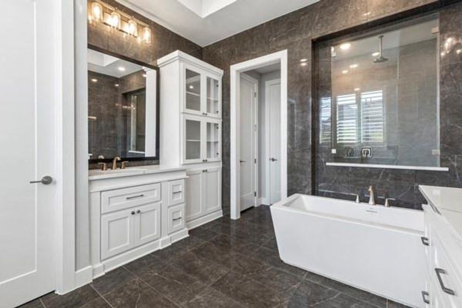 Full bath featuring vanity, tile walls, a stall shower, a freestanding tub, and dark marble finish floors Full bath featuring vanity, tile walls, a stall shower, a freestanding tub, and dark marble finish floors
