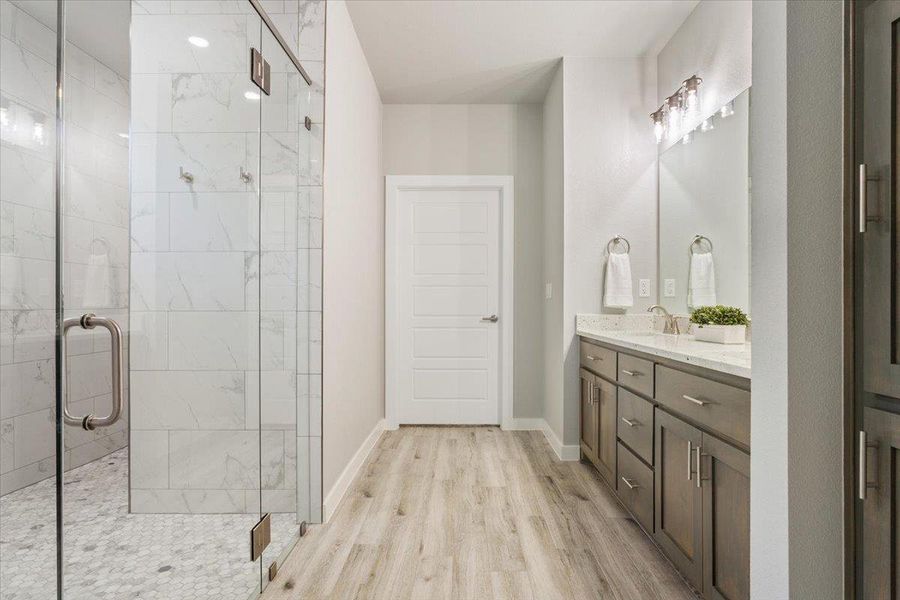 Bathroom with double vanity, a marble finish shower, and light wood-style floors Bathroom with double vanity, a marble finish shower, and light wood-style floors