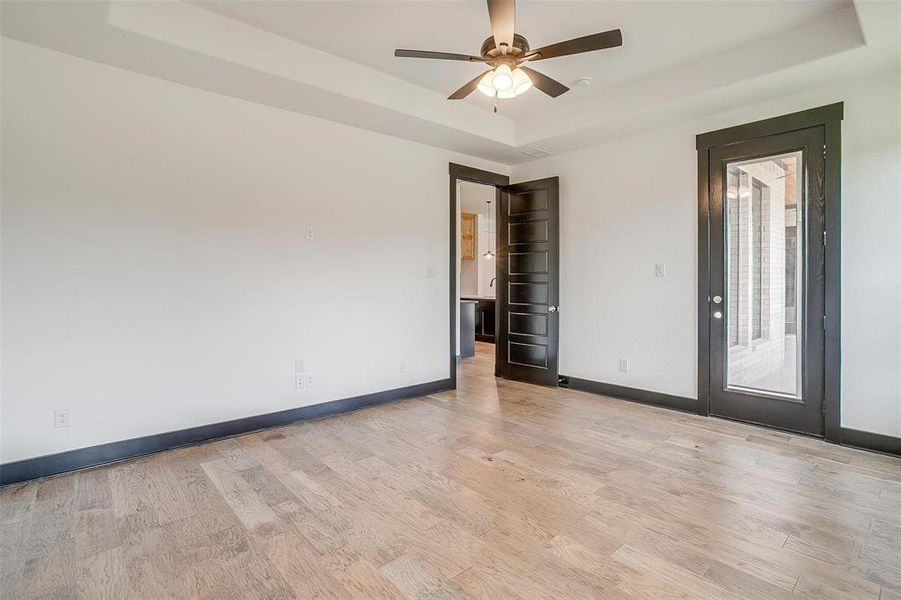 Unfurnished room with ceiling fan, a tray ceiling, and light hardwood / wood-style floors