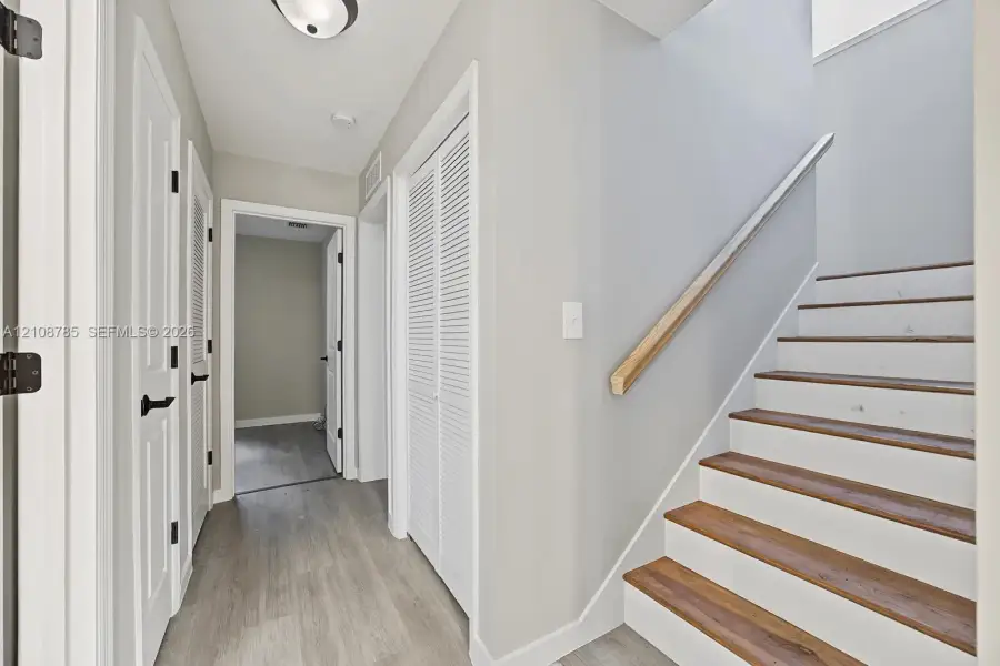 Staircase featuring wood-finish treads and a natural wood handrail, paired with interior doors showcasing matte black hardware and white louvered closet doors Staircase featuring wood-finish treads and a natural wood handrail, paired with interior doors showcasing matte black hardware and white louvered closet doors