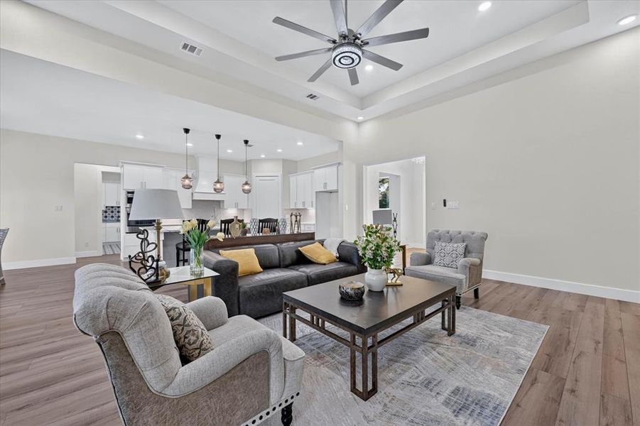 Spacious living area featuring wood-finish flooring and a tray ceiling with a ceiling fan Spacious living area featuring wood-finish flooring and a tray ceiling with a ceiling fan